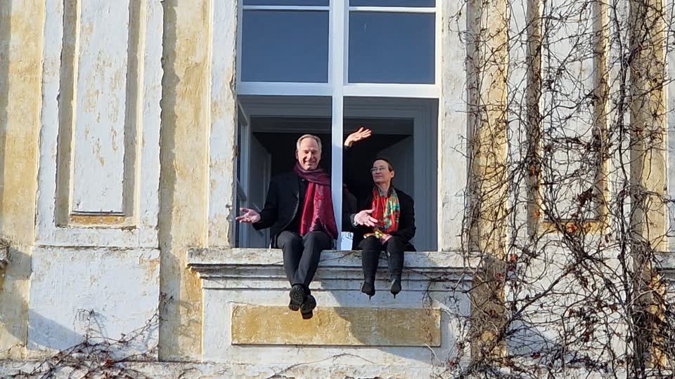 Gunhard und Sarah Keil sitzen lachend in einem offenen Fenster der Fassade von Schloss Kohfidisch, daneben wilder Wein