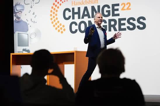 Gunhard Keil auf der Bühne des Handelsblatt Change-Kongresses 2022 mit offener Geste, im Vordergrund Zuhörende als Silhouetten
